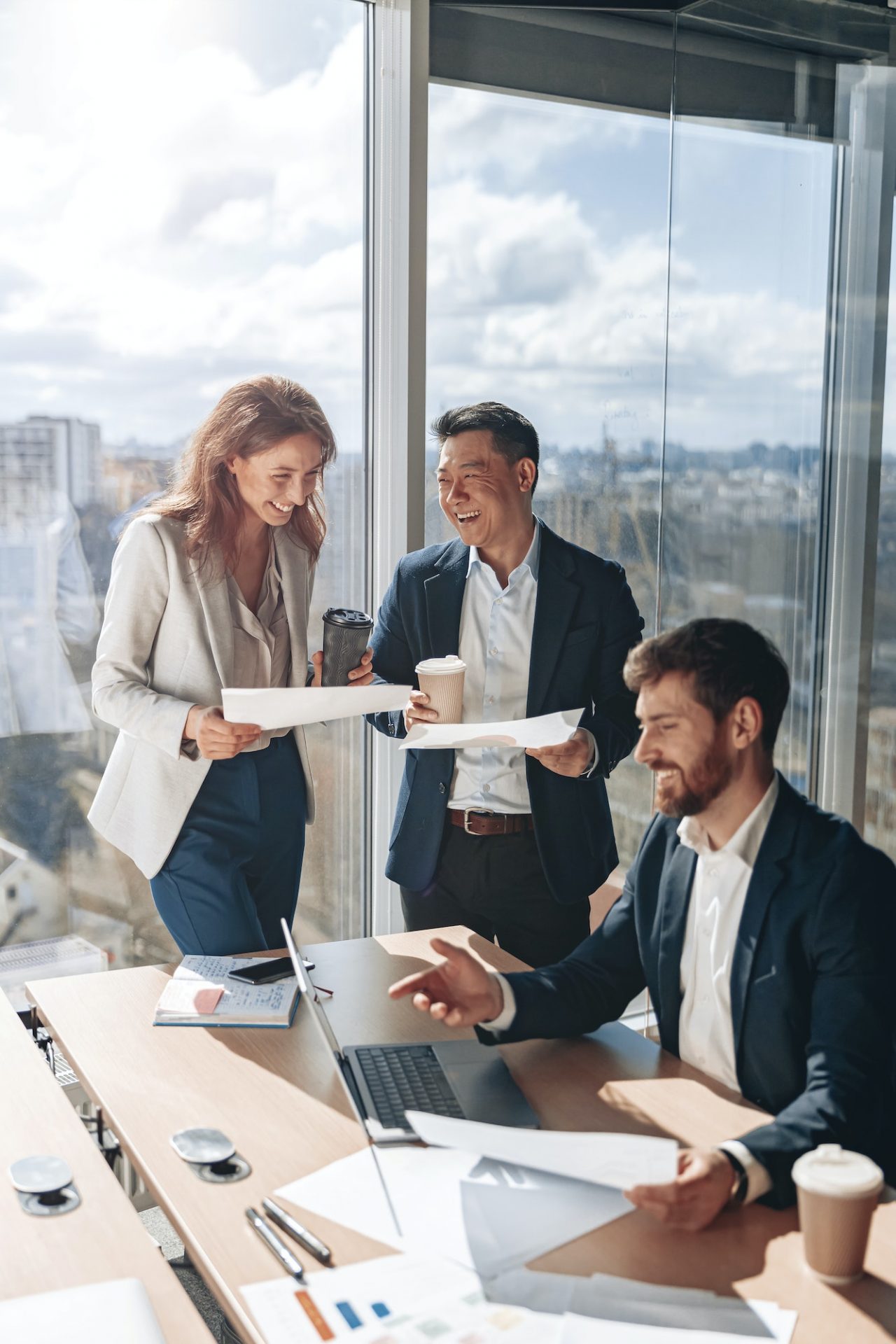 smiling businessmen drink coffee and discussing documents with graphs and charts